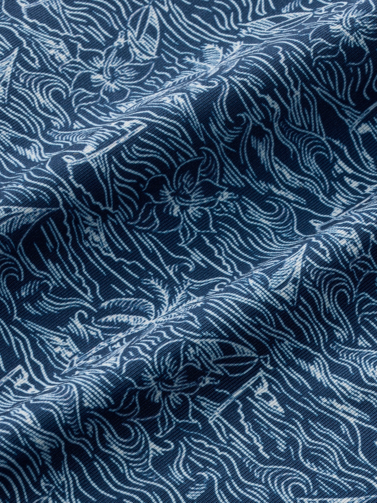 Navy blue polo shirt fabric displays an intricate white tropical leaf and vine pattern throughout.