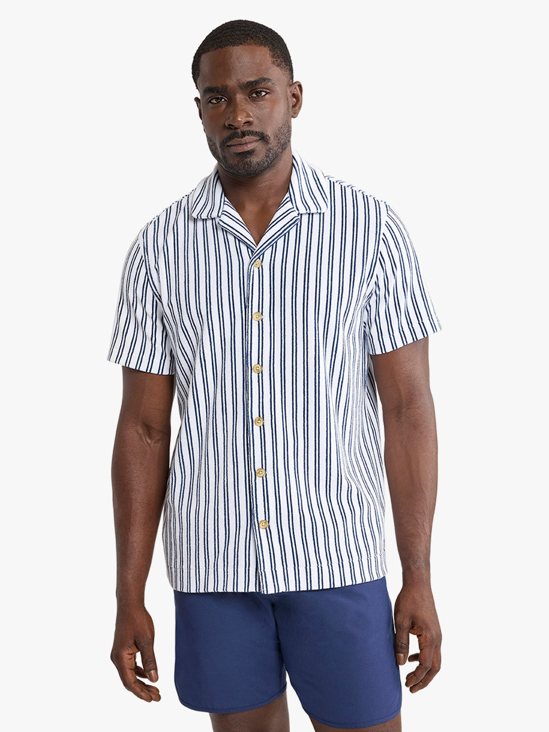 Man wearing white short-sleeve button-up shirt with navy vertical stripes and navy shorts.