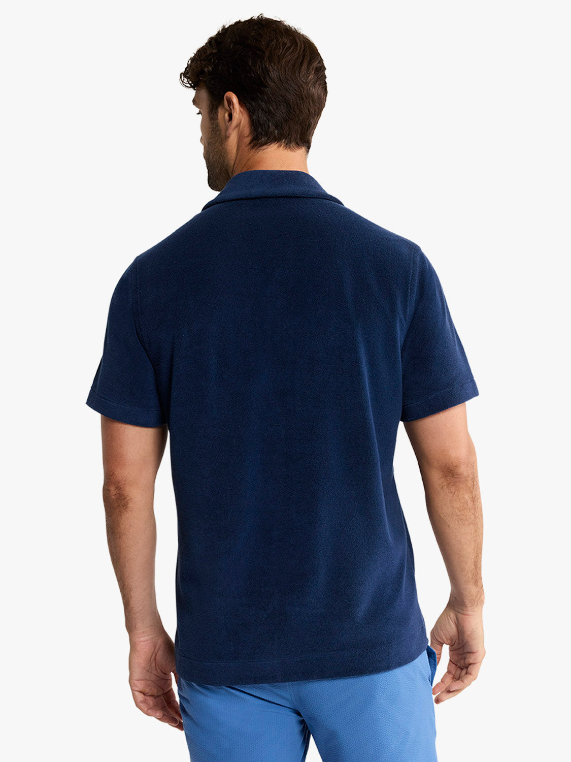 Man wearing a navy terry short sleeve button-up shirt, shown from behind against a white background.
