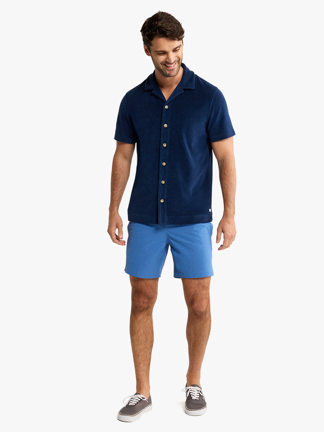 Man wearing navy terry short sleeve button up shirt with gold buttons and blue shorts.