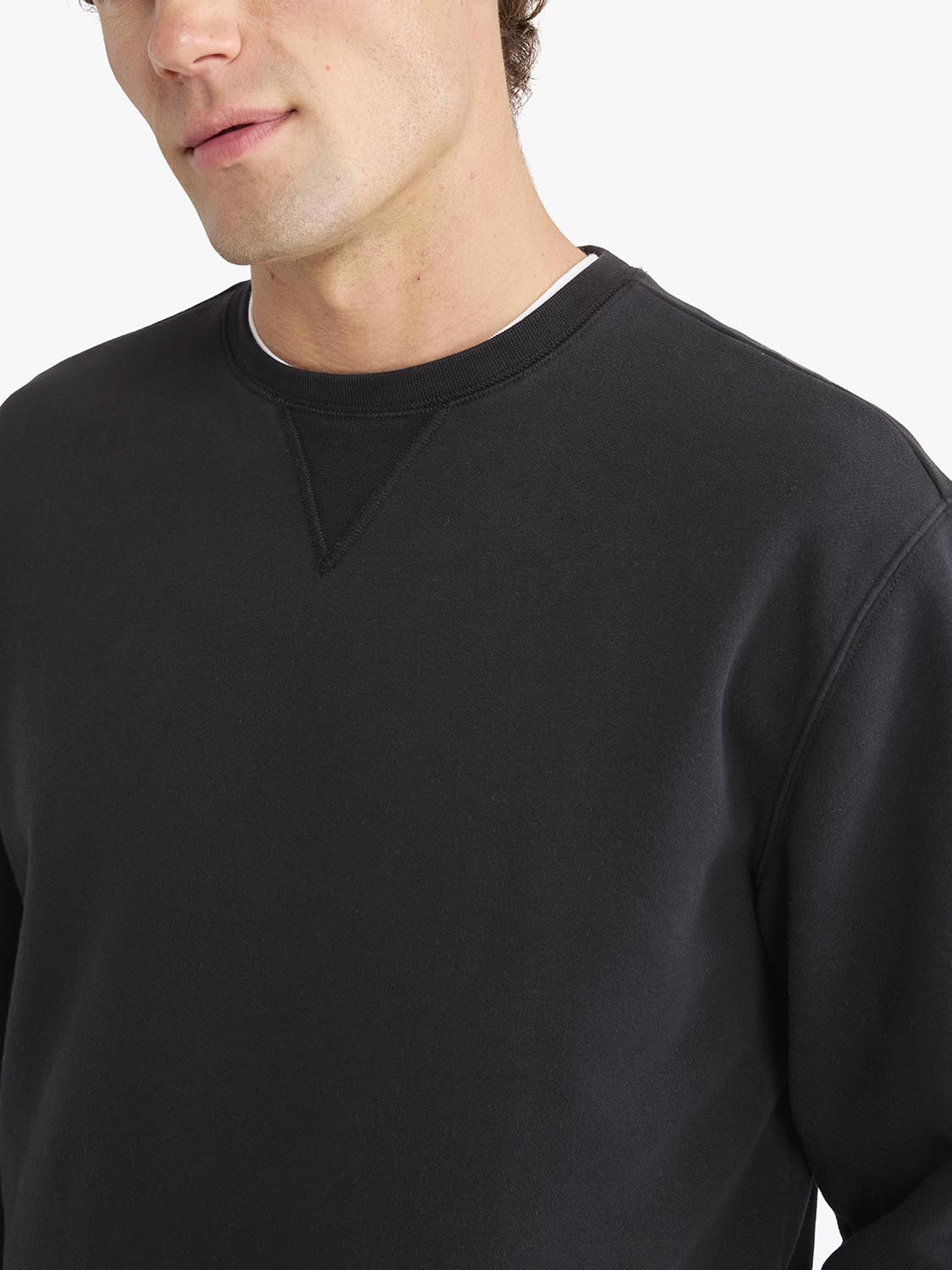 Man wearing a black crewneck sweatshirt with ribbed collar and cuffs details.
