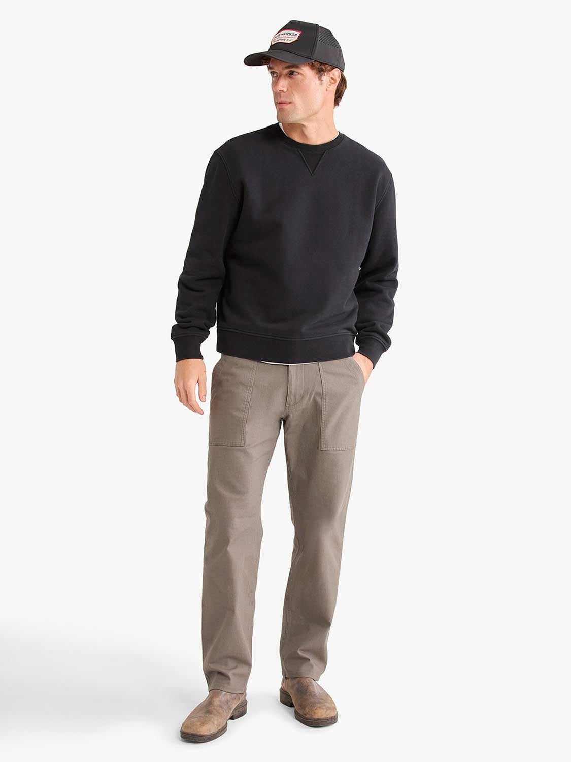 Man wearing a black crewneck sweatshirt with khaki pants and a black cap.