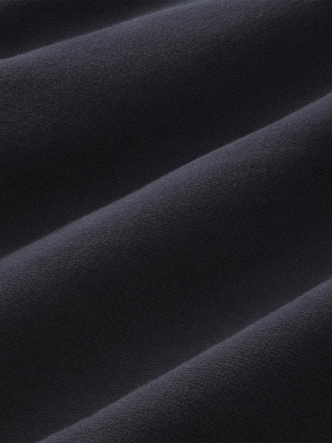 Close-up of black crewneck sweatshirt fabric showing textured knit material with diagonal folds.