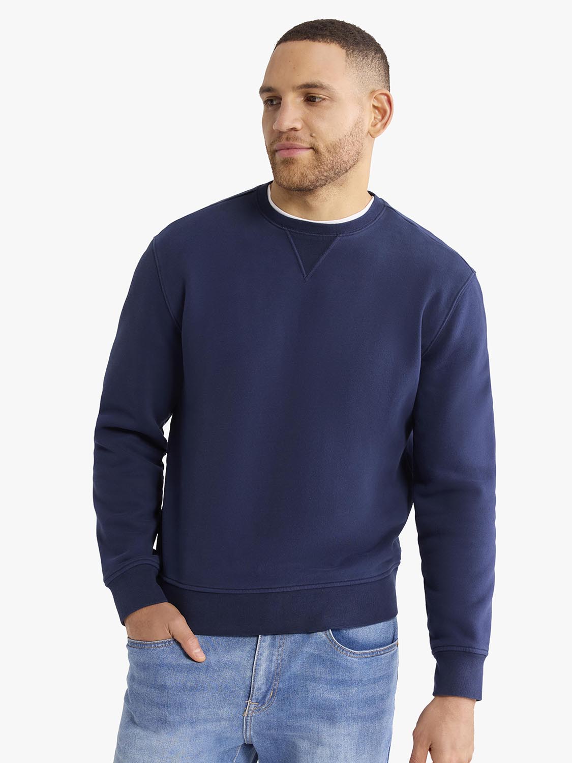 Man wearing a navy crewneck sweatshirt with ribbed cuffs and blue jeans.