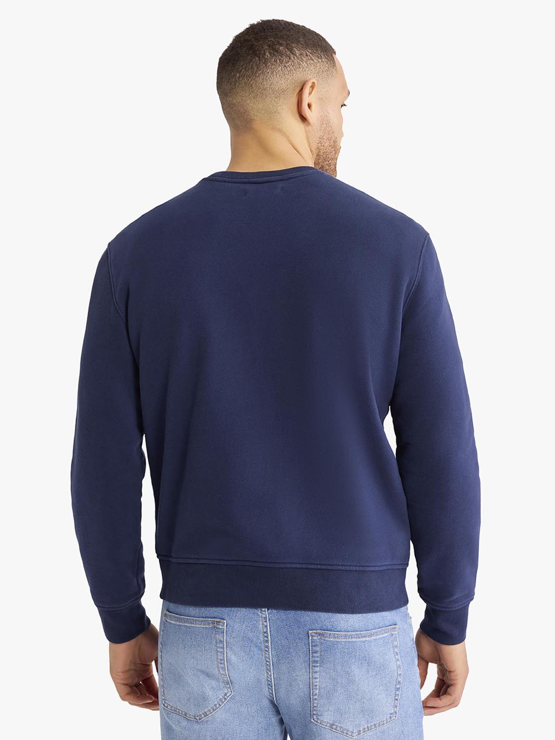 Man wearing navy crewneck sweatshirt viewed from back, paired with light blue jeans.