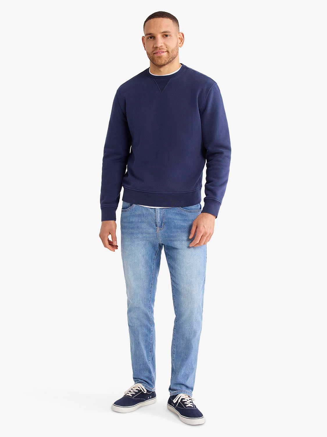 Man wearing a navy crewneck sweatshirt with light blue jeans and dark sneakers.
