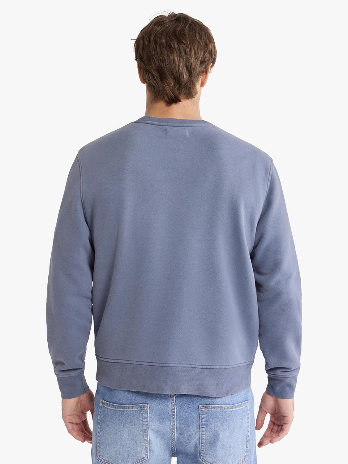Man wearing a dusty blue crewneck sweatshirt and light blue jeans, shown from the back.