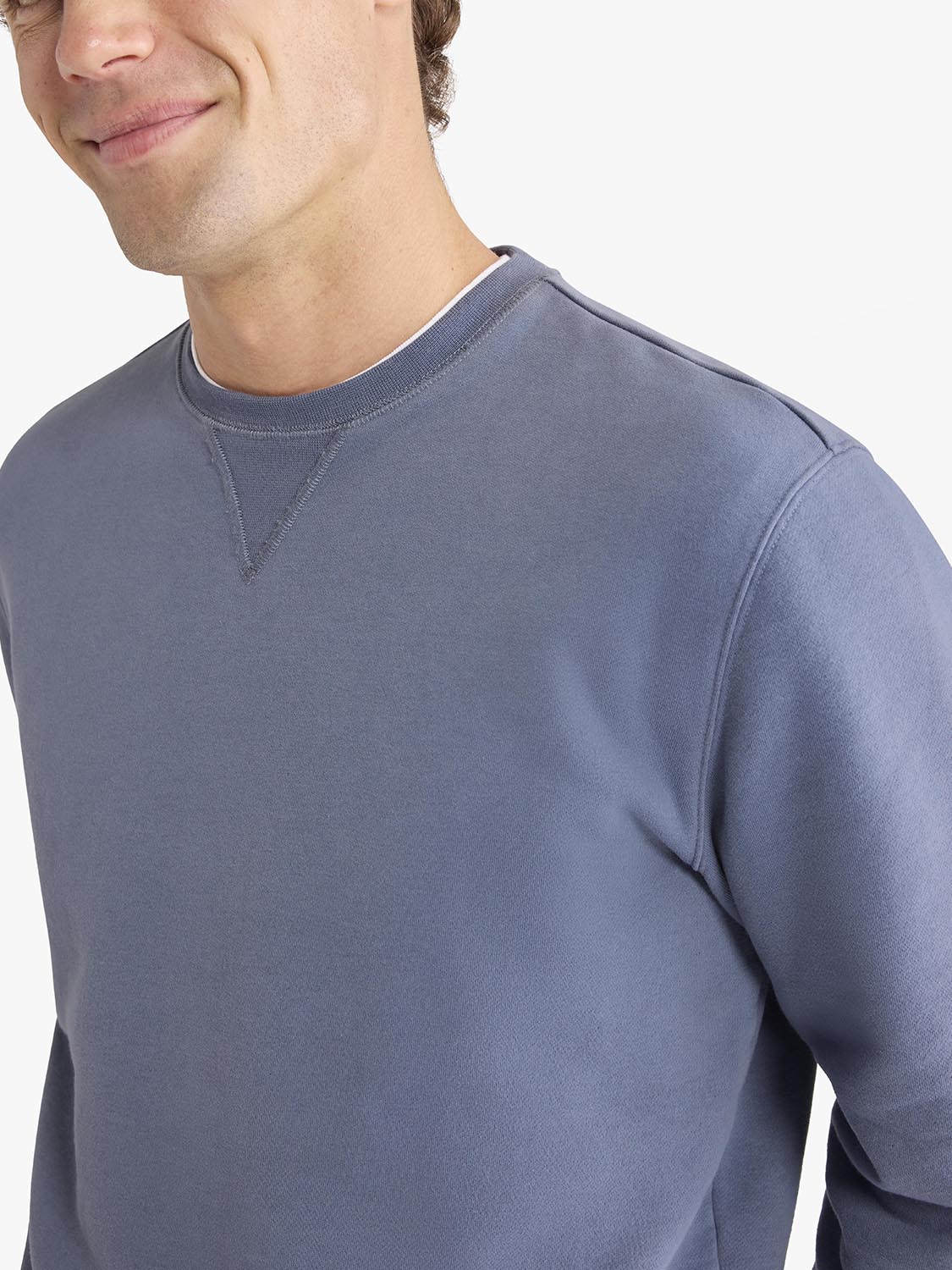 Man wearing a blue-grey crewneck sweatshirt with ribbed trim details and long sleeves.