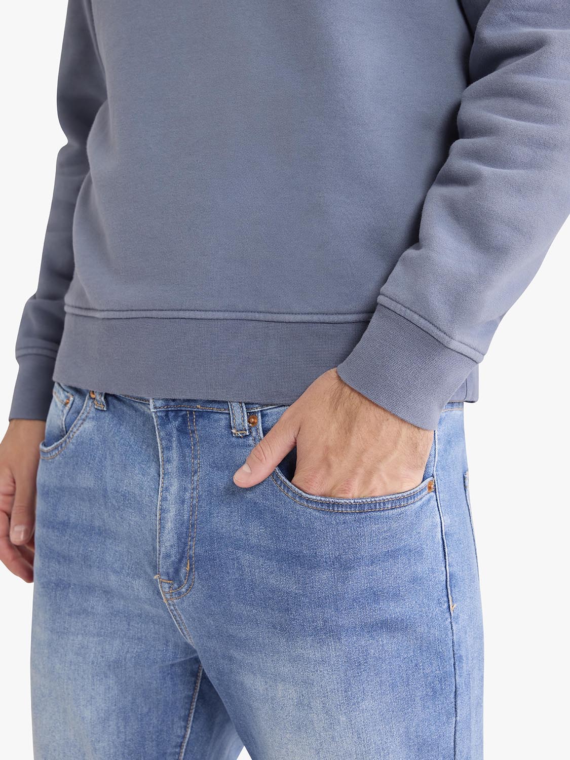 Person wearing a gray crewneck sweatshirt with ribbed cuffs tucked into blue jeans.