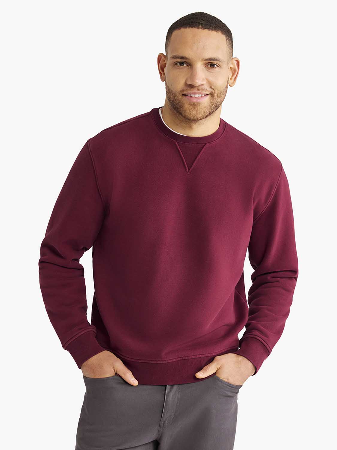 Man wearing a burgundy crewneck sweatshirt with long sleeves and gray pants.