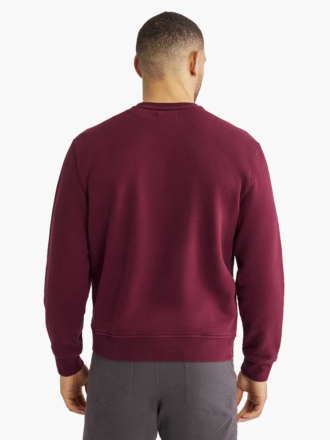Man wearing a burgundy crewneck sweatshirt with long sleeves and gray pants, shown from behind.