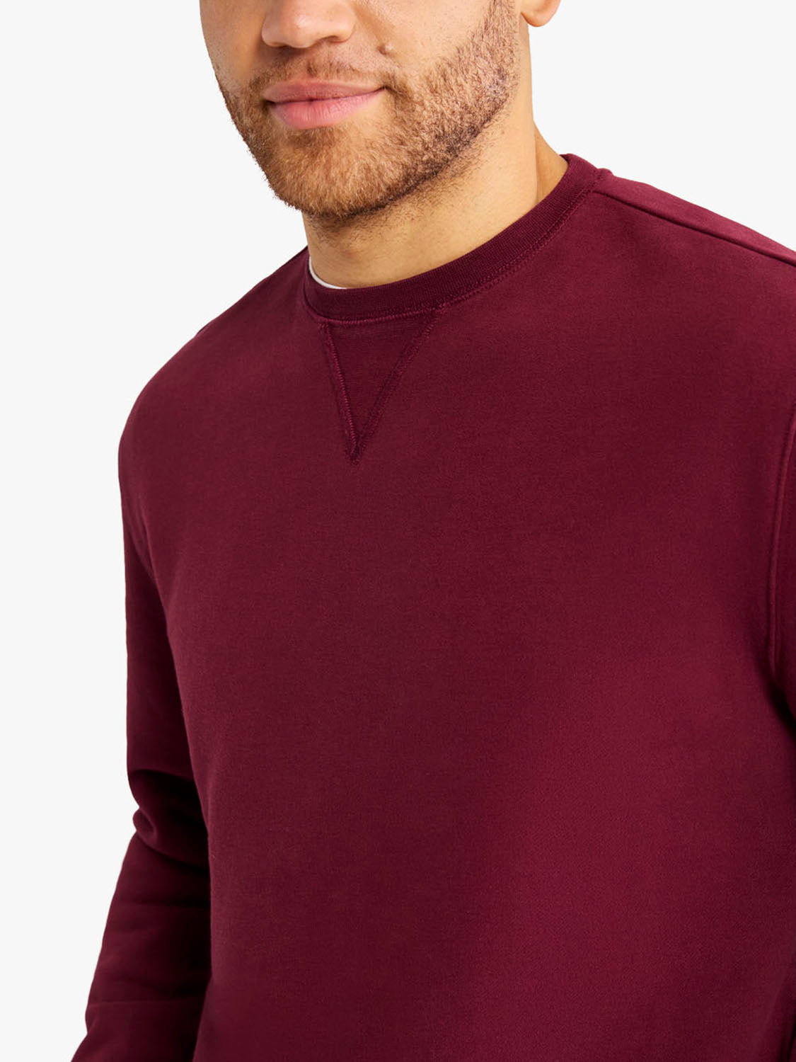 Man wearing a burgundy crewneck sweatshirt with long sleeves and ribbed neckline detail.