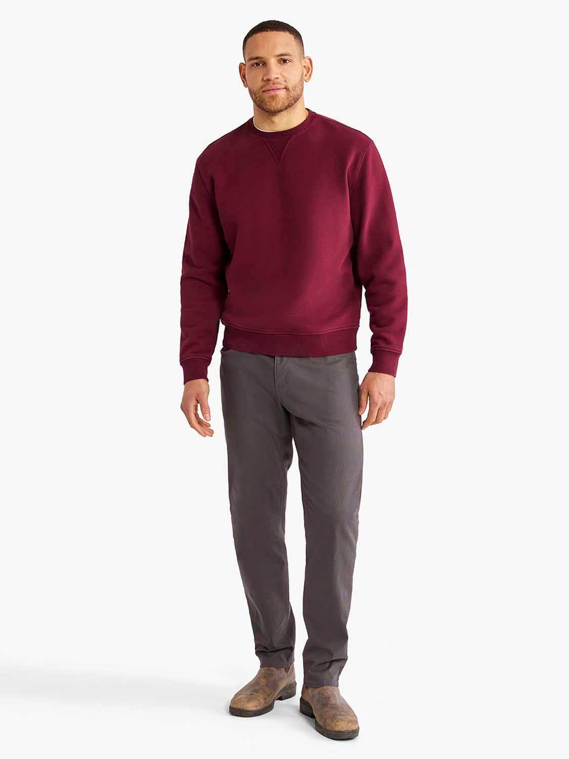 Man wearing a burgundy crewneck sweatshirt with gray pants and brown boots.