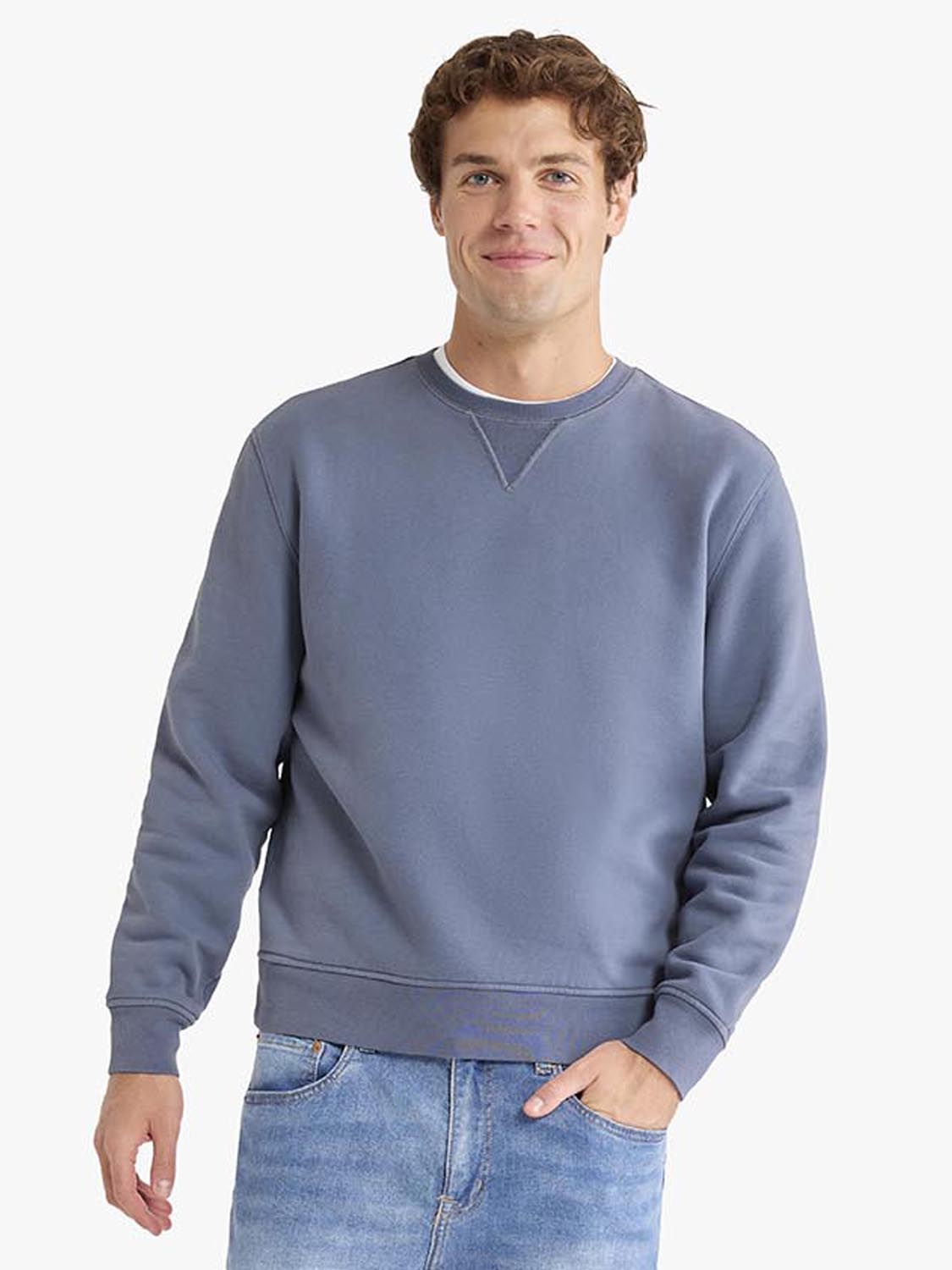 Man wearing a blue-gray crewneck sweatshirt with ribbed cuffs and a contrasting neckline.