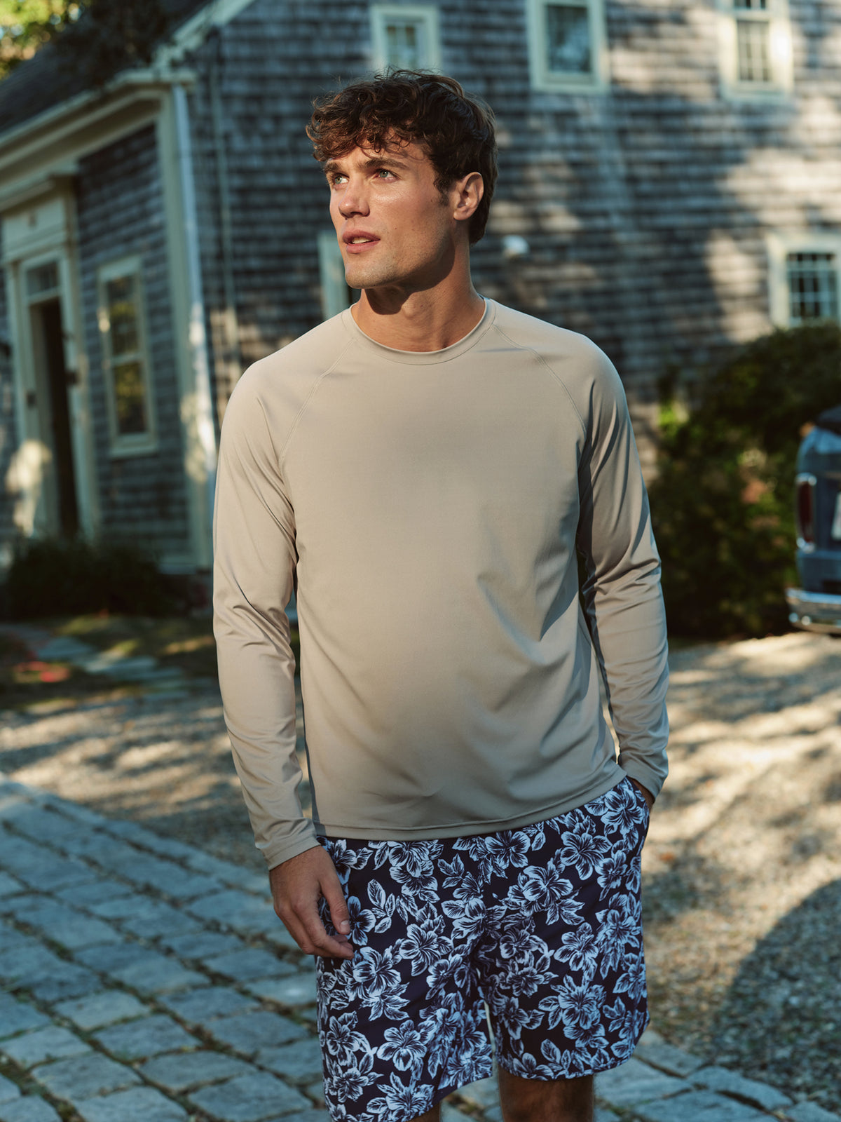 Man wearing a white long-sleeve rashguard and patterned swim shorts standing outdoors.