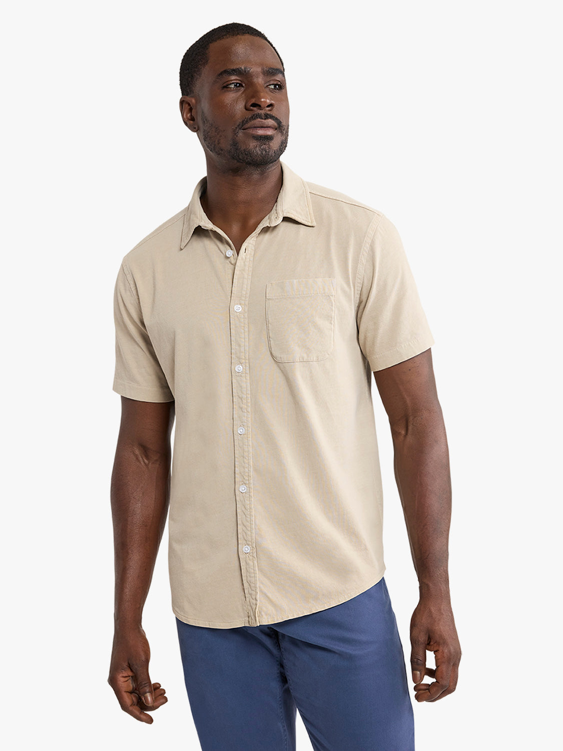 Man wearing a beige short-sleeved button-up shirt with a chest pocket and navy trousers.