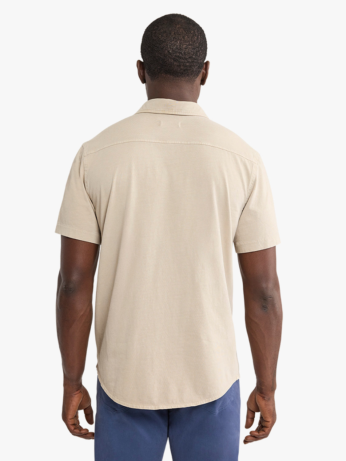 Man wearing a cream-colored short-sleeve button-up shirt with navy pants, photographed from behind.