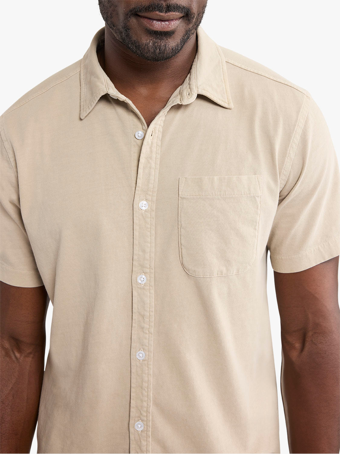 Man wearing a beige short-sleeve button-up shirt with a chest pocket and white buttons.