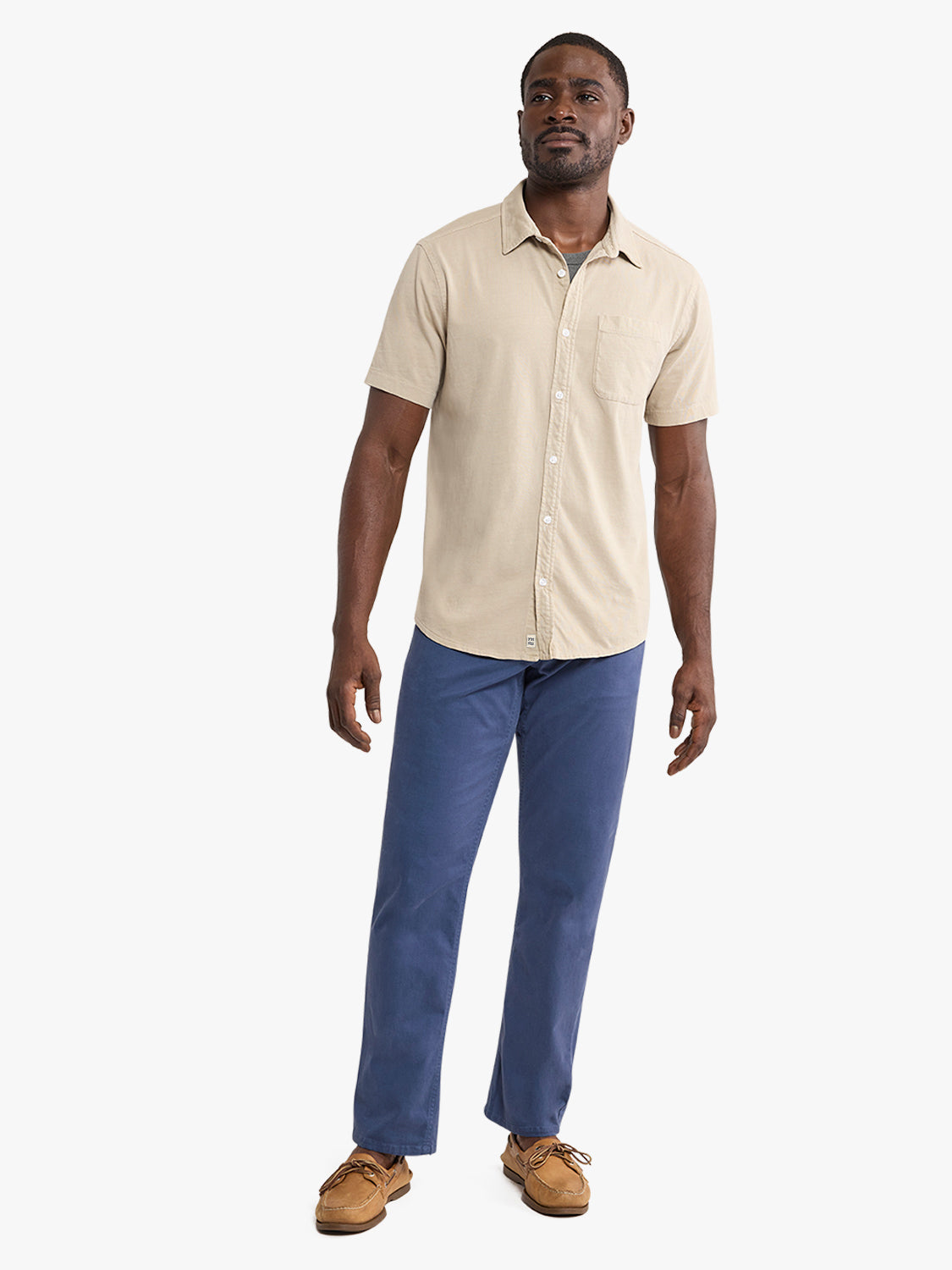 Man wearing a cream-colored short-sleeved button-up shirt with chest pocket and blue jeans.