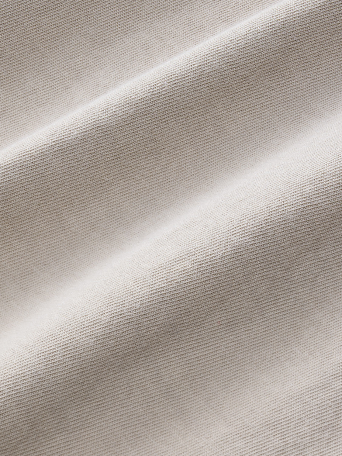 Close-up detail of shell-colored textured fabric with a fine woven pattern and natural draping.