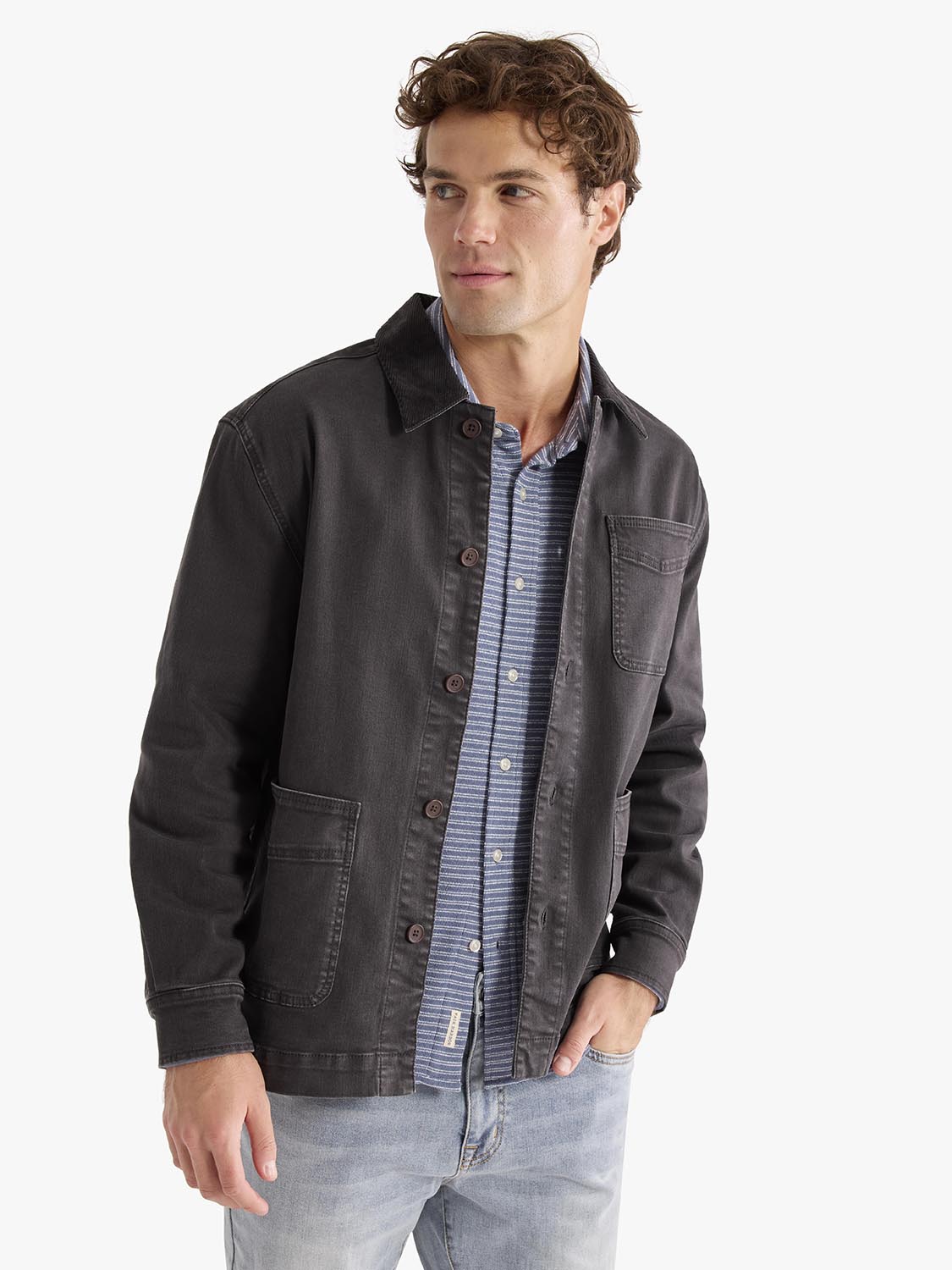 Man wearing a black denim chore jacket over a blue striped shirt and light blue jeans.
