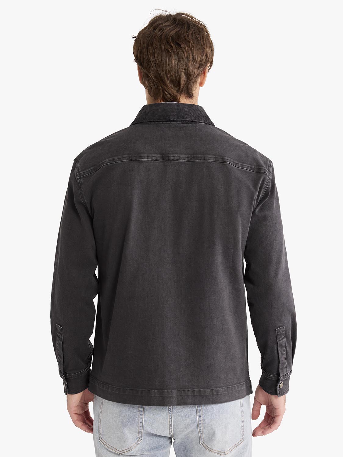 Man wearing black chore jacket with collar and button cuffs over light jeans, viewed from behind.