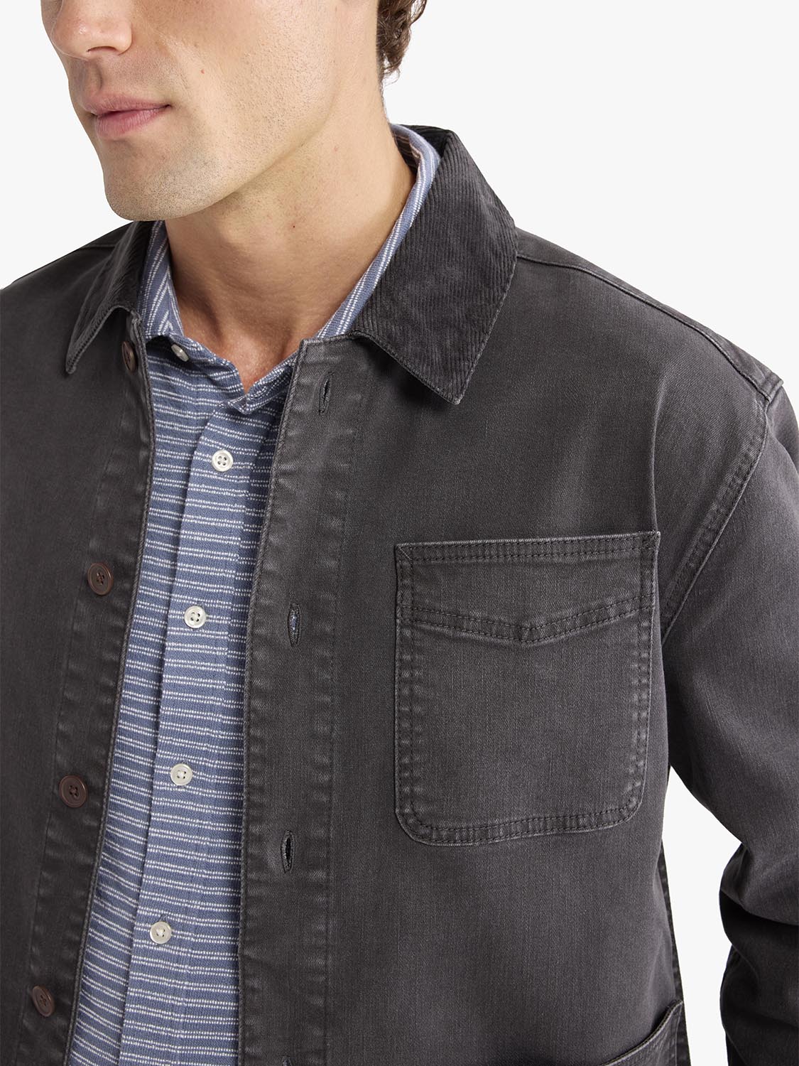 Man wearing a black chore jacket with a chest pocket over a blue striped shirt.