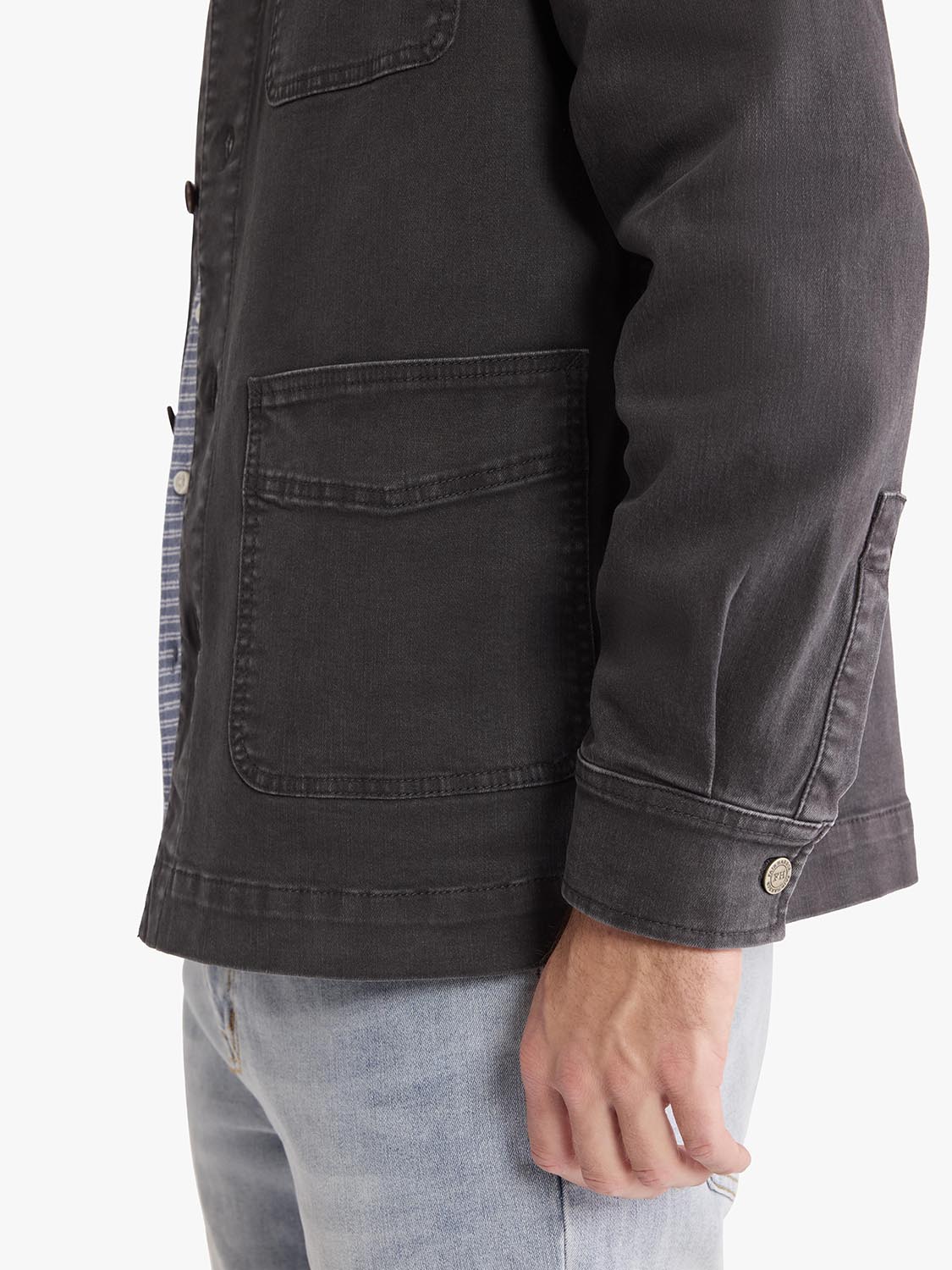Black denim chore jacket with large front pockets and button cuffs worn over light blue jeans.