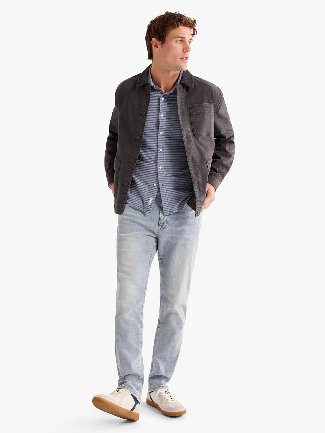Man wearing a black chore jacket over a blue striped shirt with light jeans.