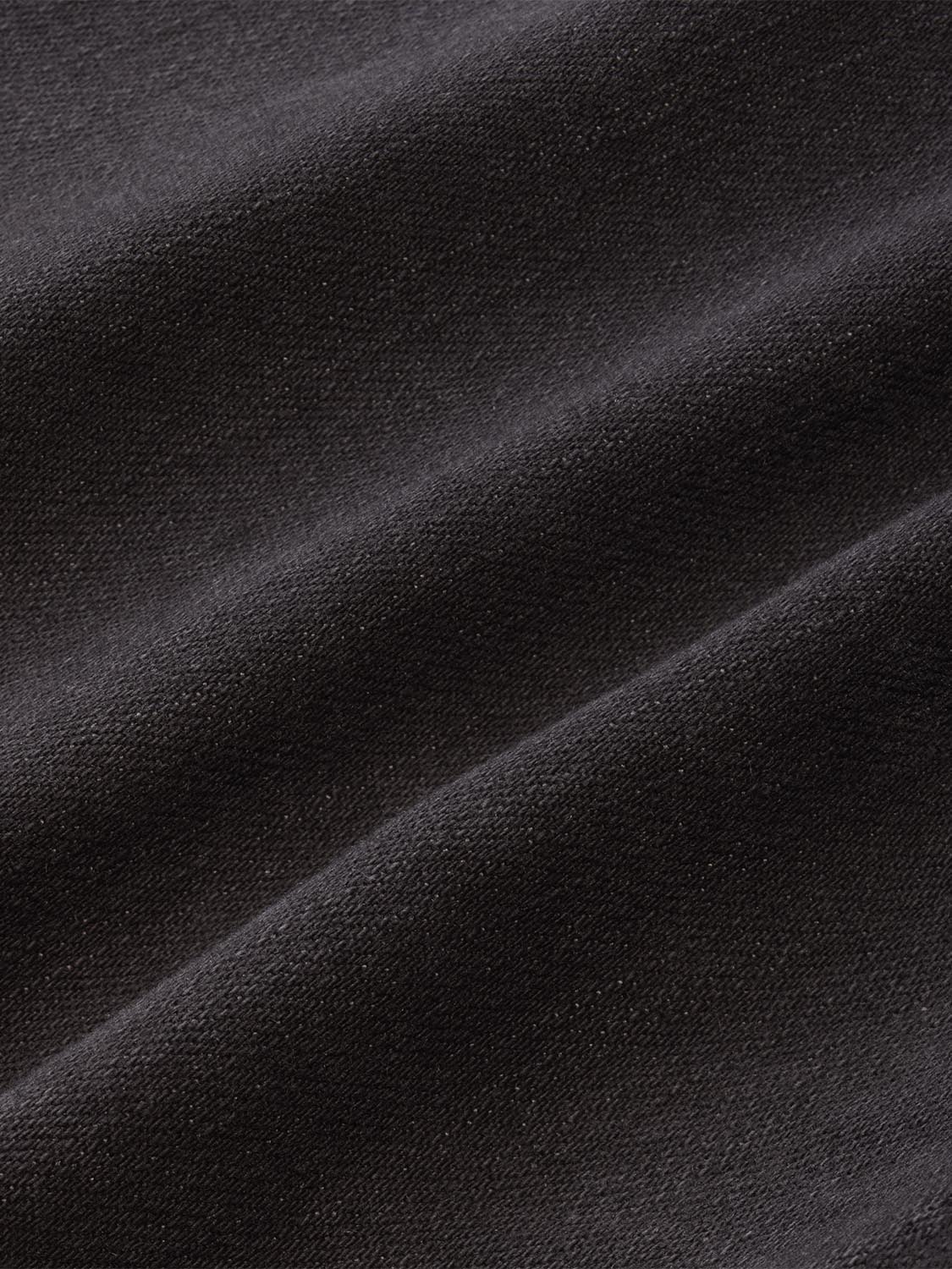 Black textured fabric with diagonal seams creating a folded, dimensional surface pattern.