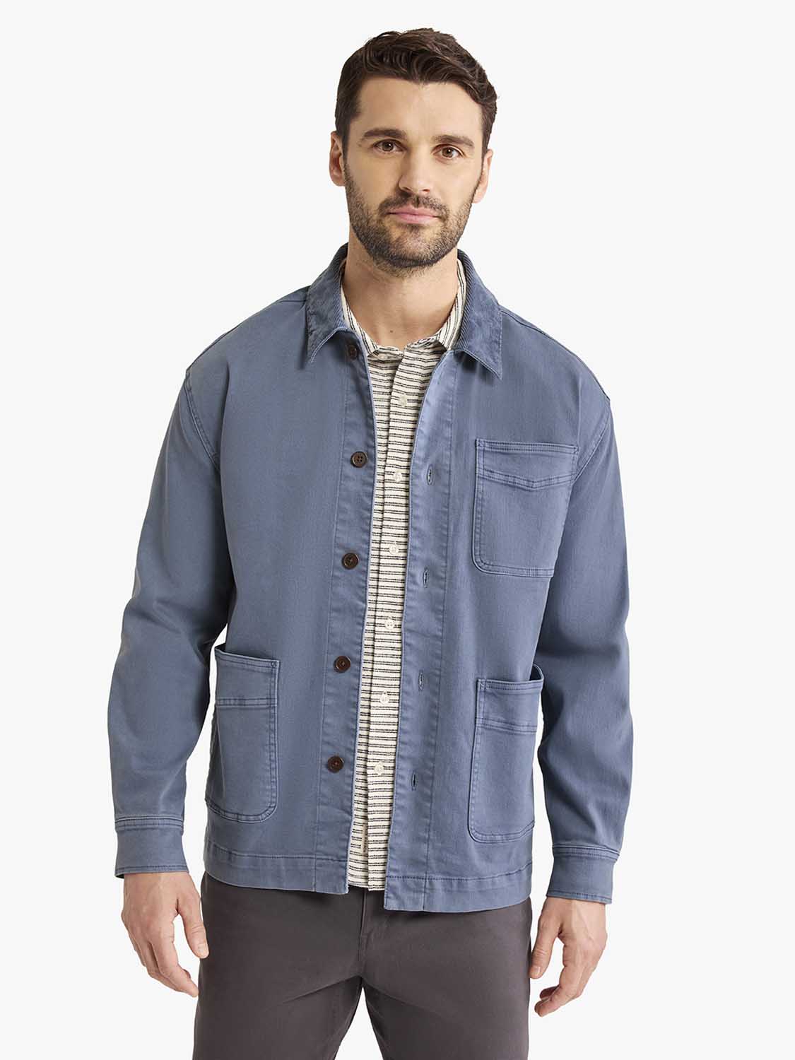 Man wearing a blue cotton chore jacket with brown buttons and chest pockets over a striped shirt.
