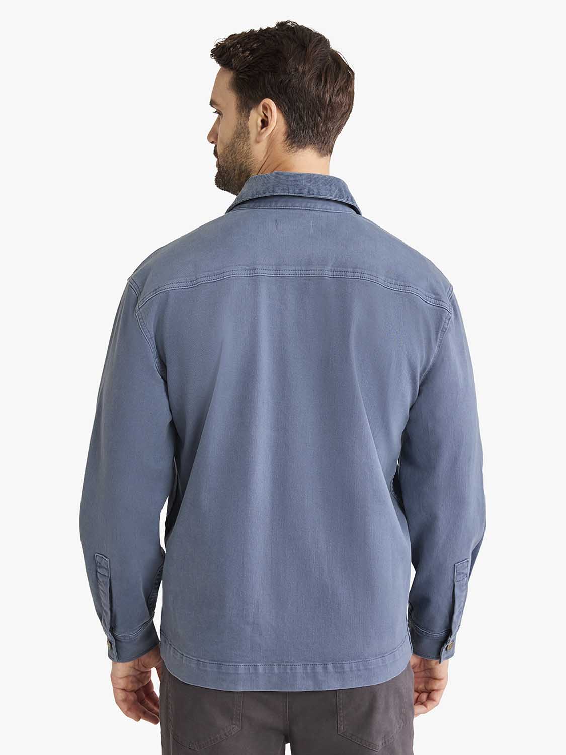 Man wearing blue chambray chore jacket with collar and long sleeves shown from behind.