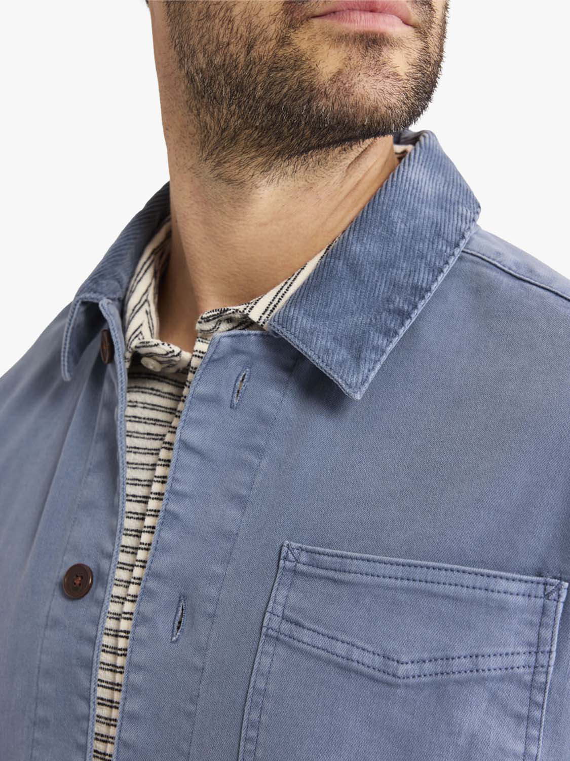 Man wearing a blue chore jacket with brown buttons and a striped shirt underneath.