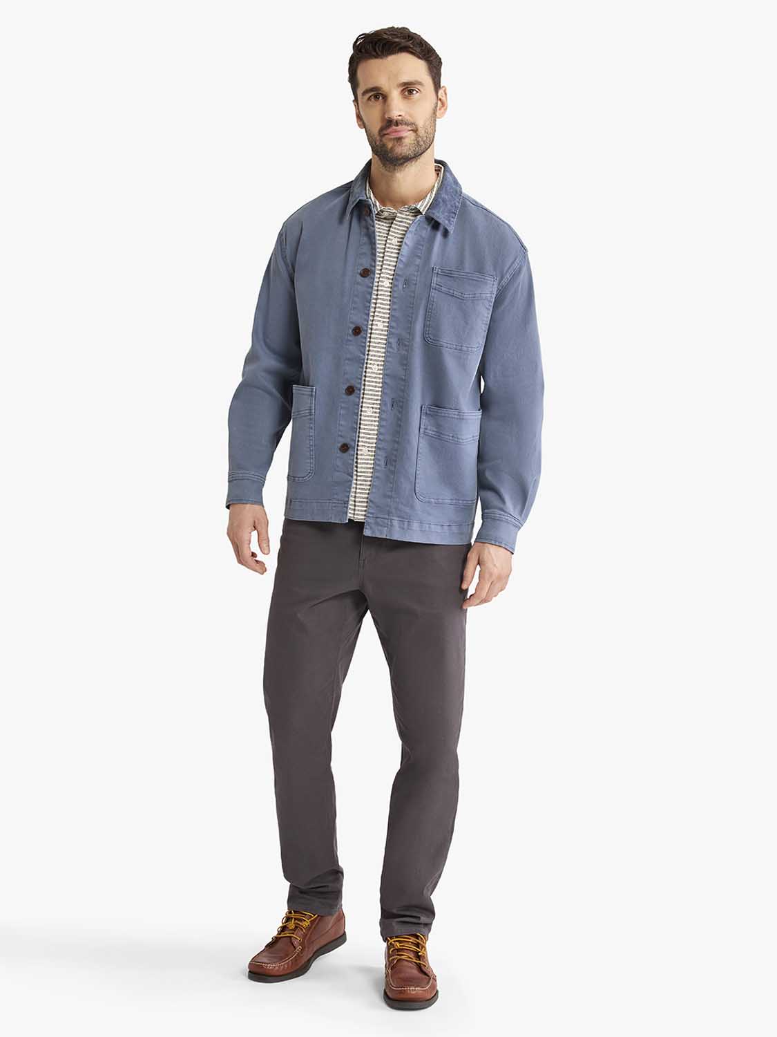 Man wearing a blue denim chore jacket with button front and patch pockets over a striped shirt.