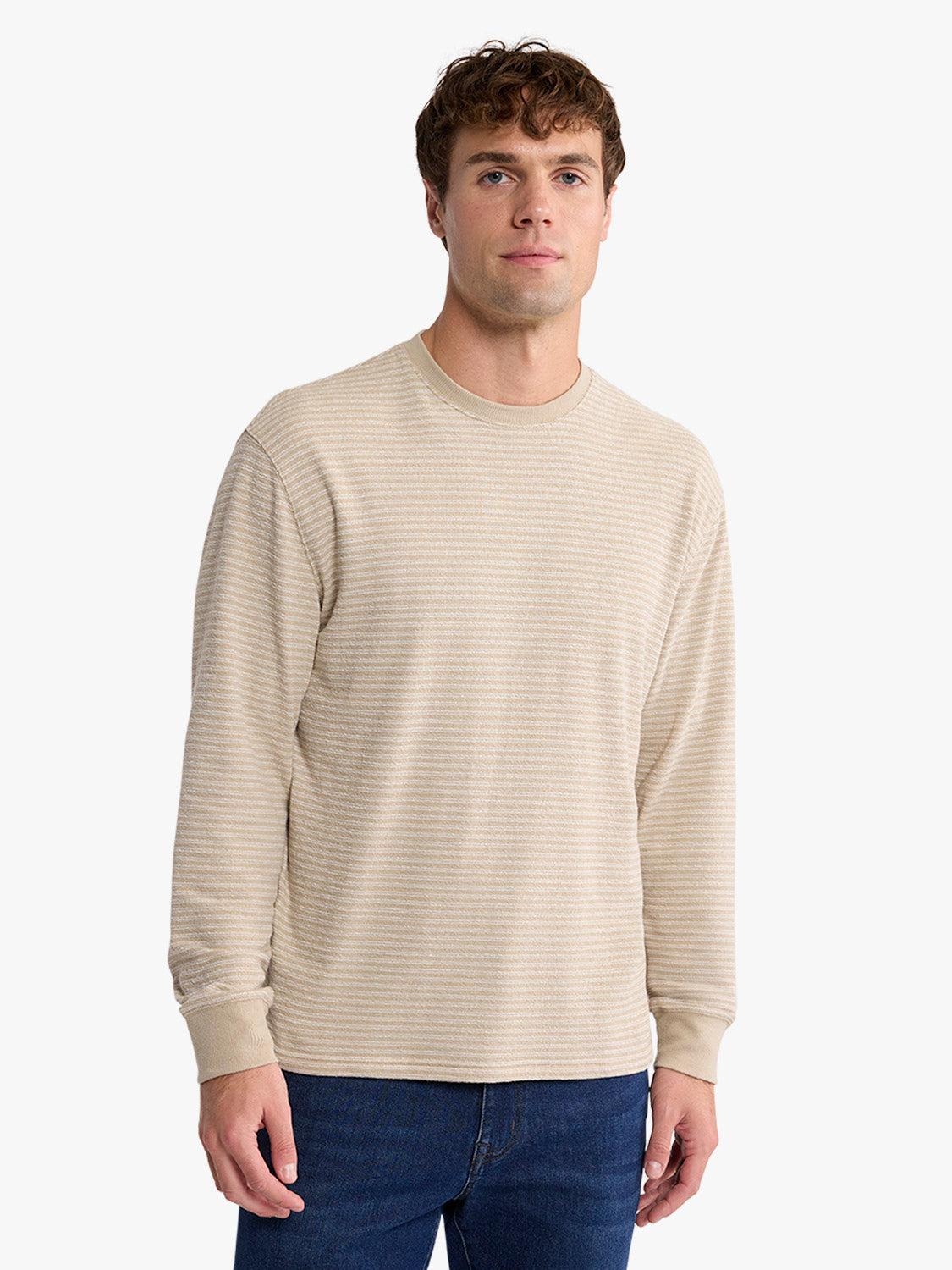 Man wearing a natural-colored long-sleeve crewneck sweatshirt with horizontal texture paired with dark jeans.