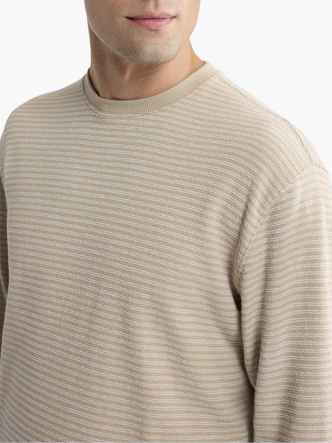 Man wearing a natural beige crewneck sweater with horizontal textured ribbing throughout.