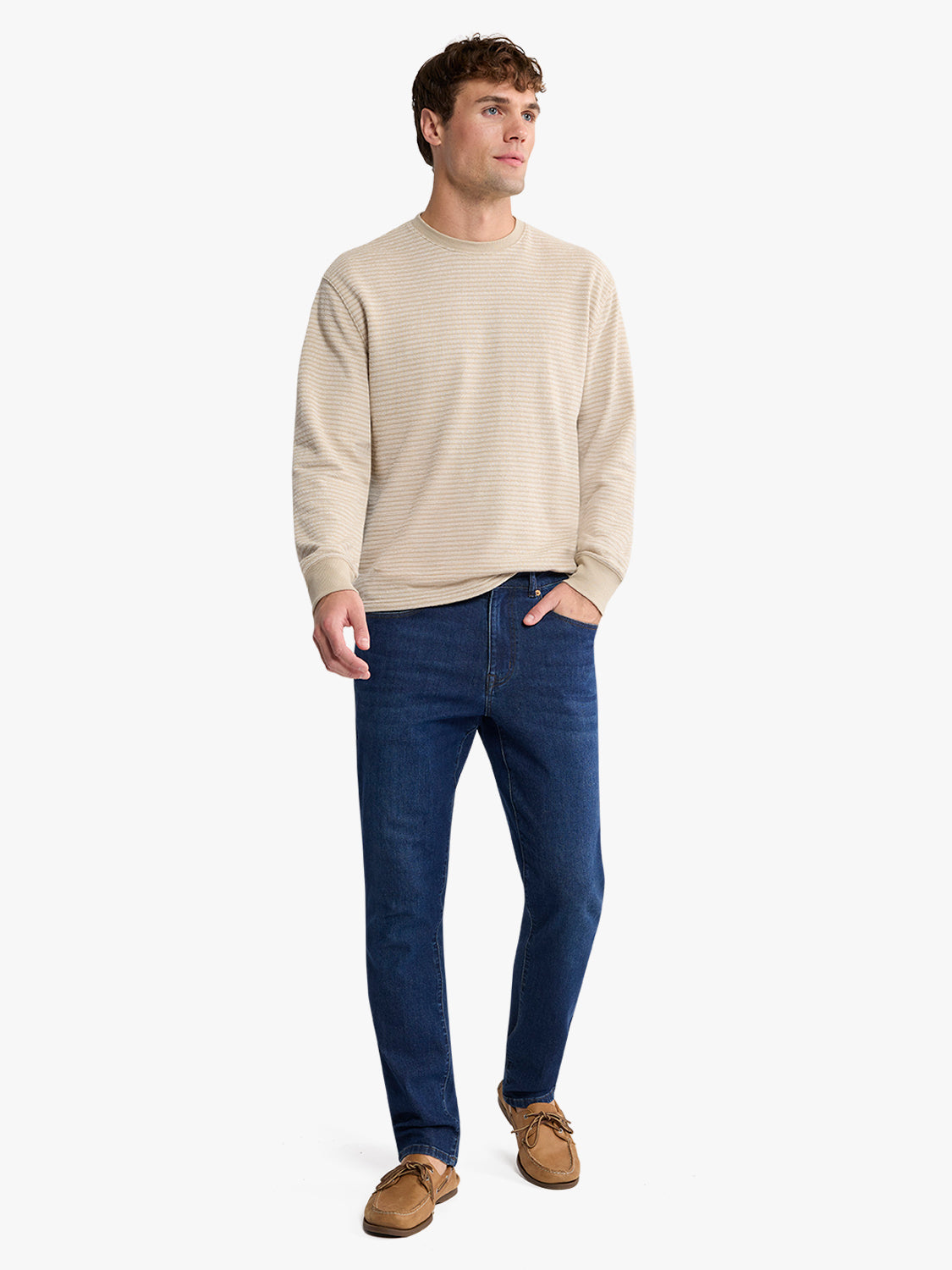Man wearing a natural striped crewneck sweatshirt with dark jeans and tan loafers.