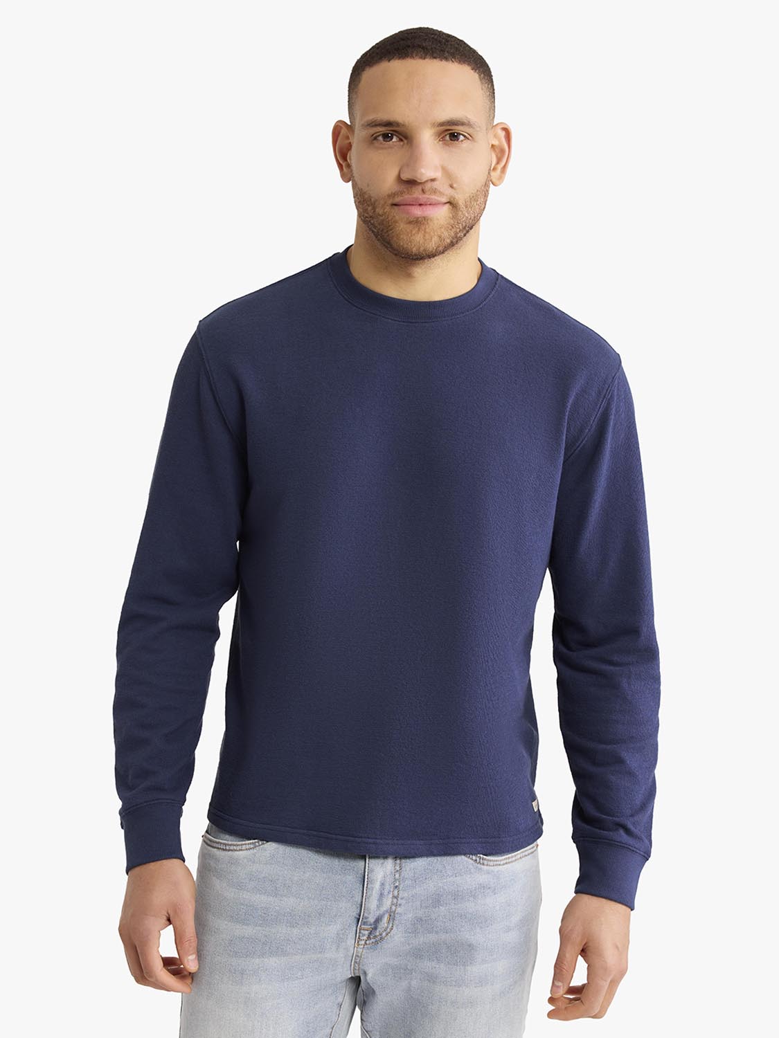 Man wearing a navy blue crewneck sweatshirt with long sleeves and light blue jeans.