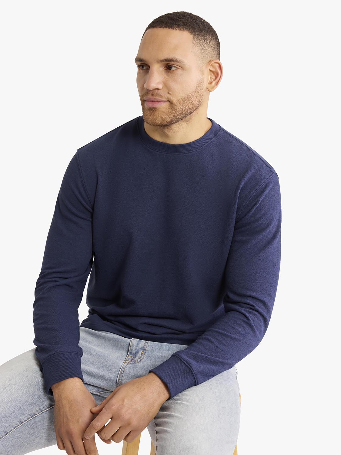 Man wearing a navy blue crewneck sweatshirt with long sleeves and light wash jeans.