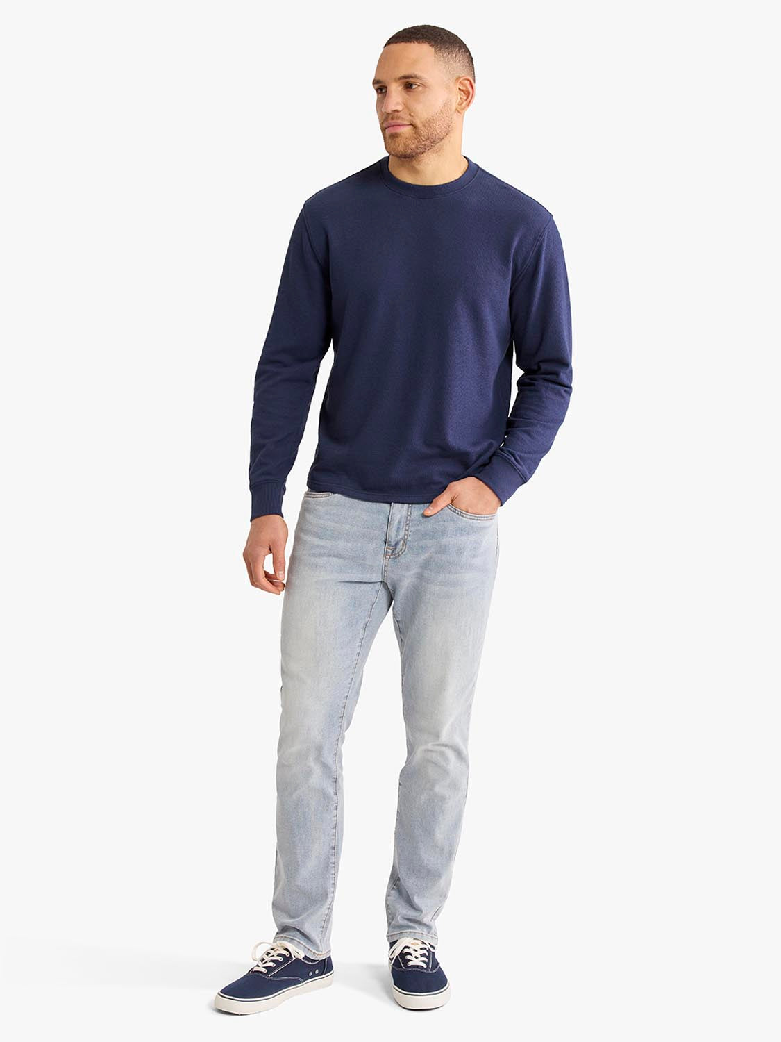 Man wearing a navy crewneck sweatshirt with light blue jeans and navy sneakers.