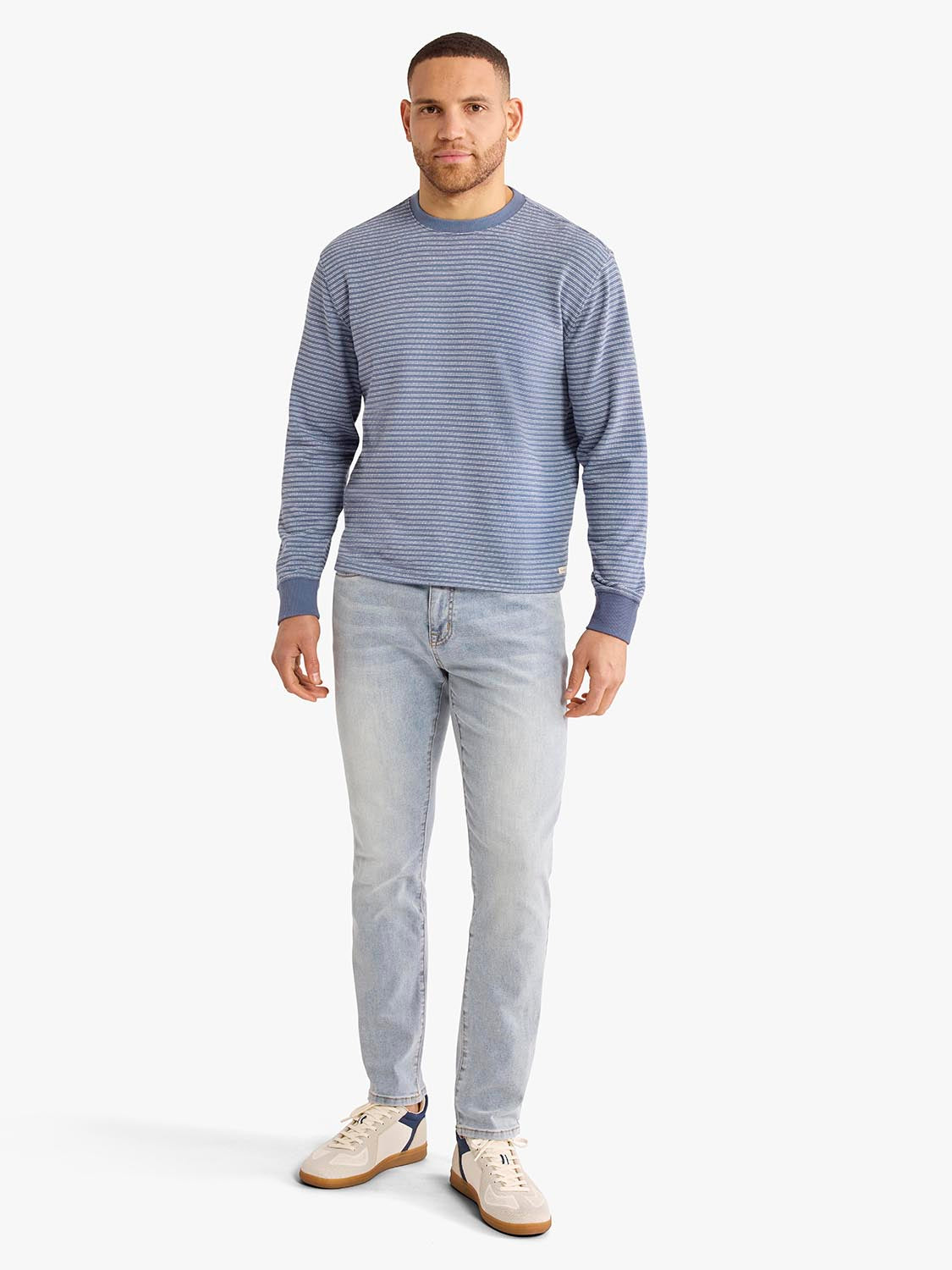 Man wearing a blue and gray horizontal striped crewneck sweatshirt with light wash jeans.