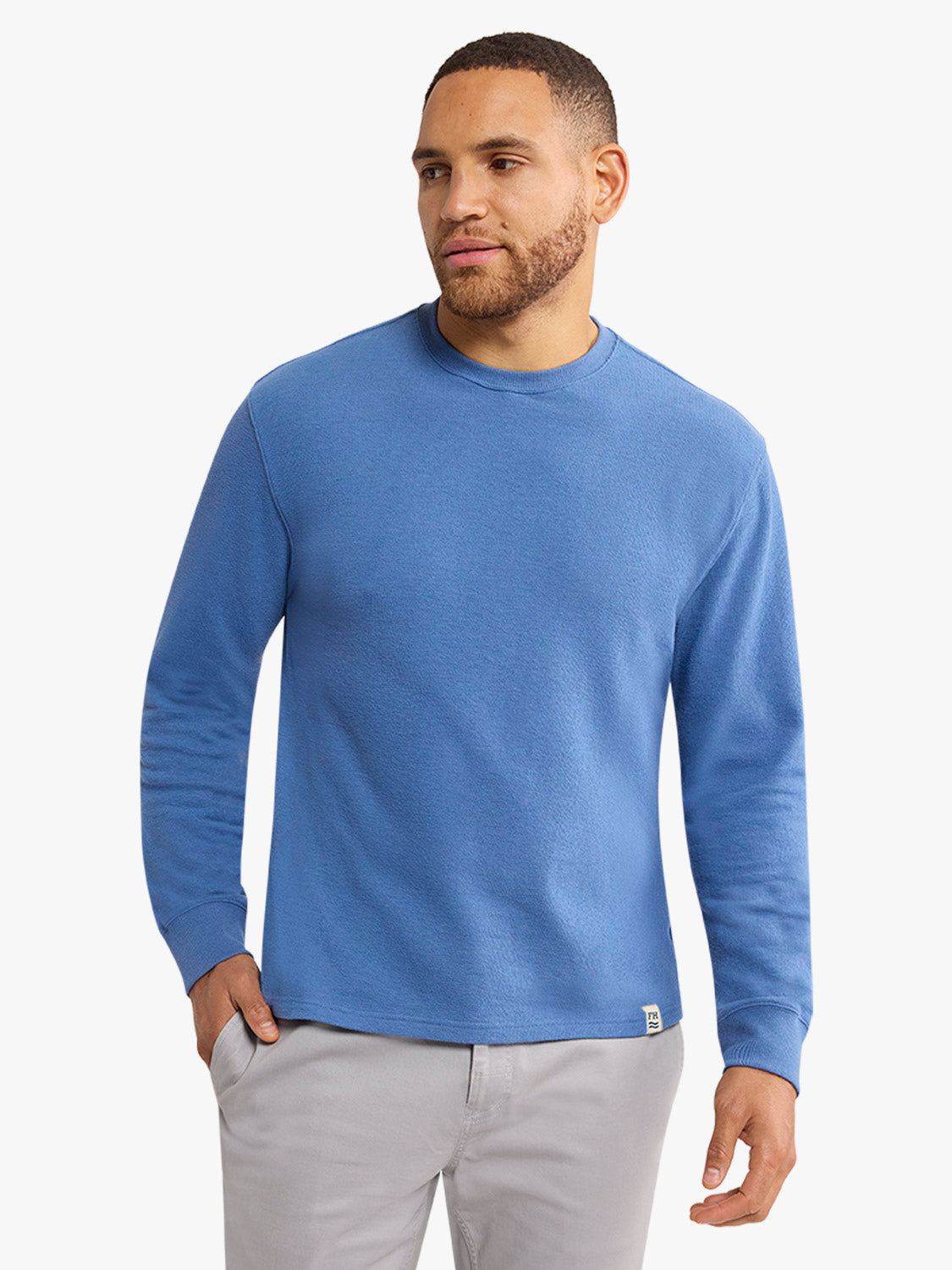 Man wearing a sea blue terry crewneck sweatshirt with long sleeves and gray pants.