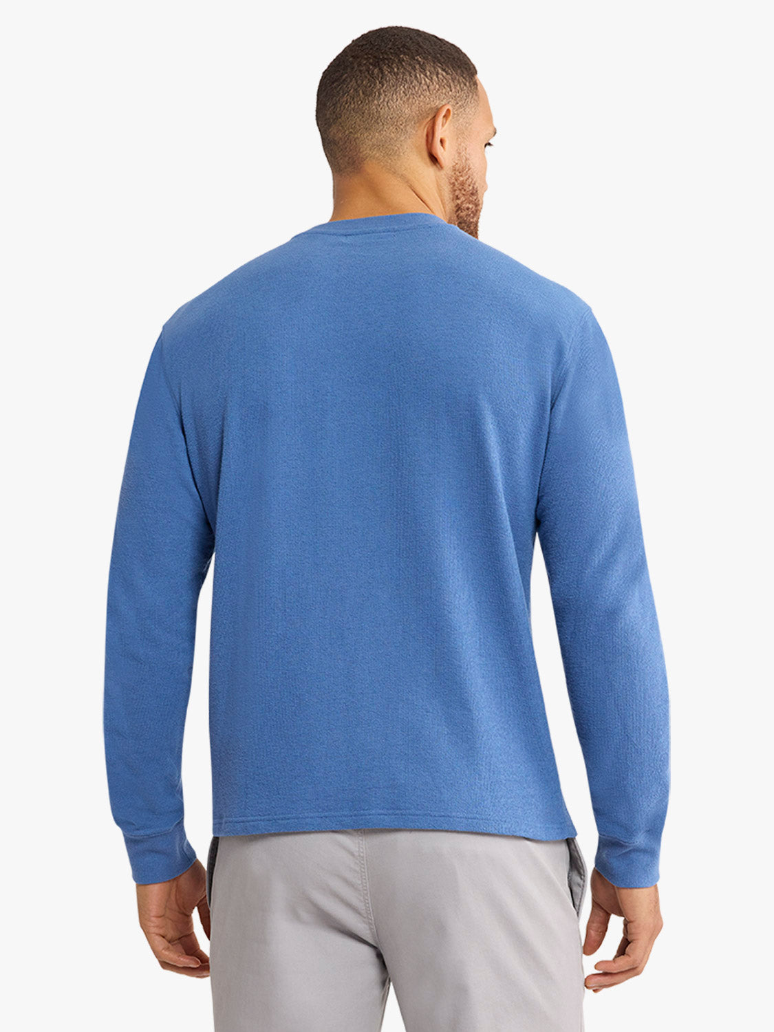 Man wearing a sea blue crewneck sweatshirt with long sleeves and gray pants, shown from behind.