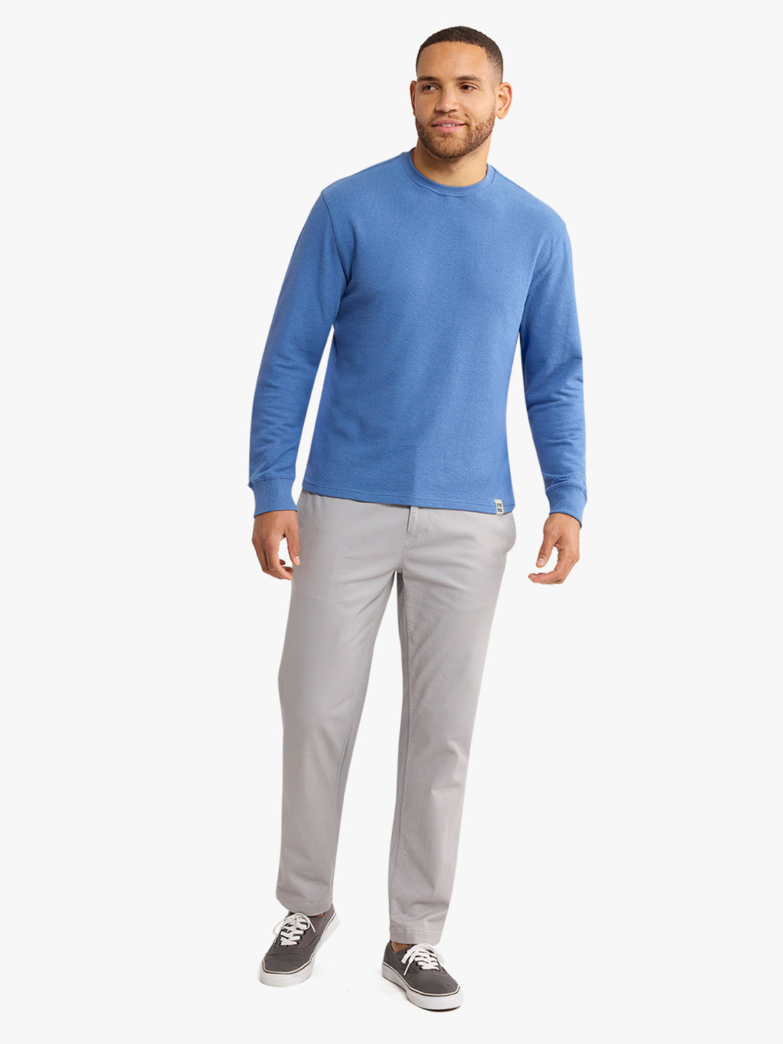 Man wearing a sea blue crewneck sweatshirt with gray pants and dark sneakers.