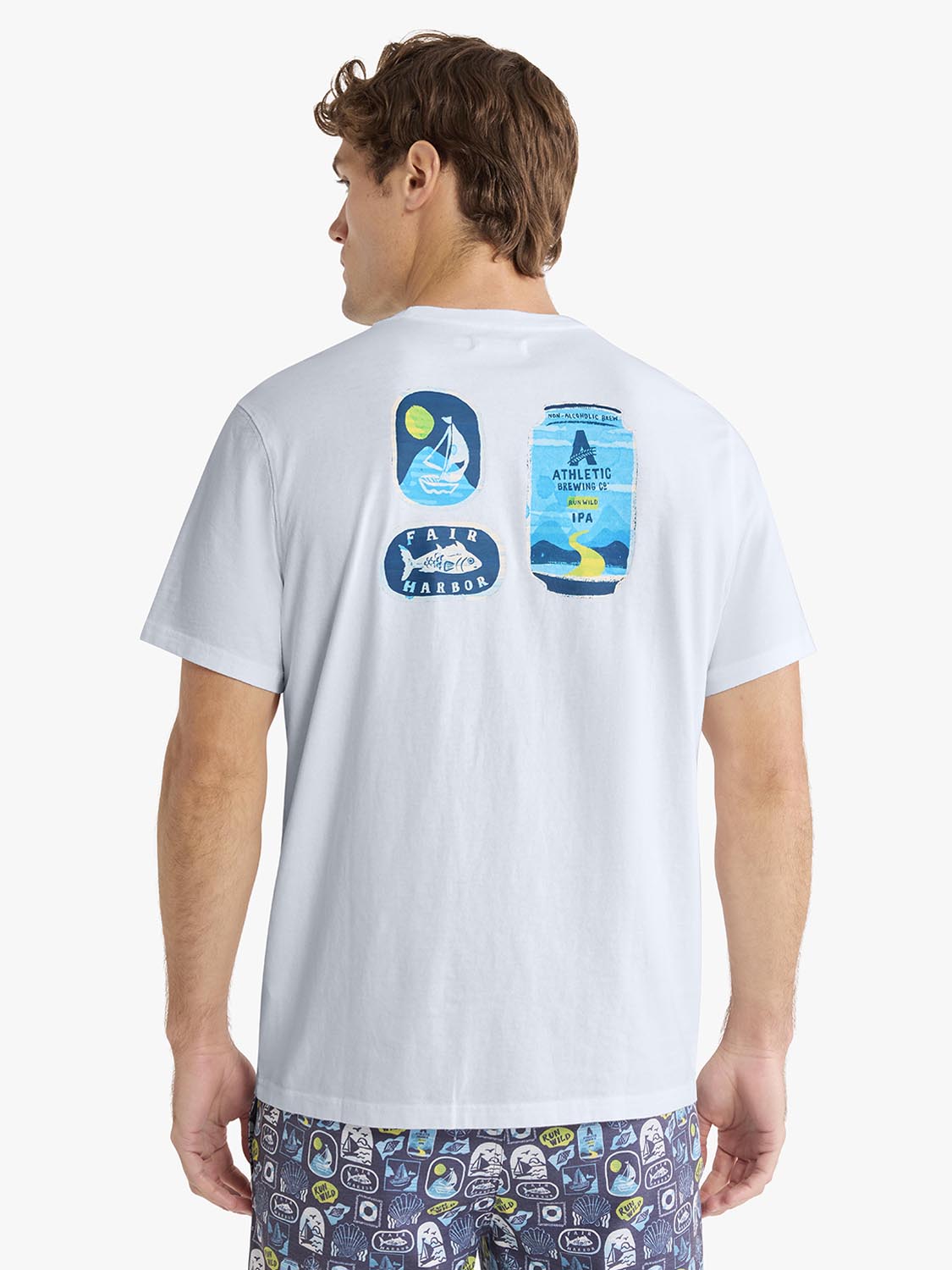 Man wearing light blue graphic t-shirt with sailboat, beer can, and harbor logos printed on the back.