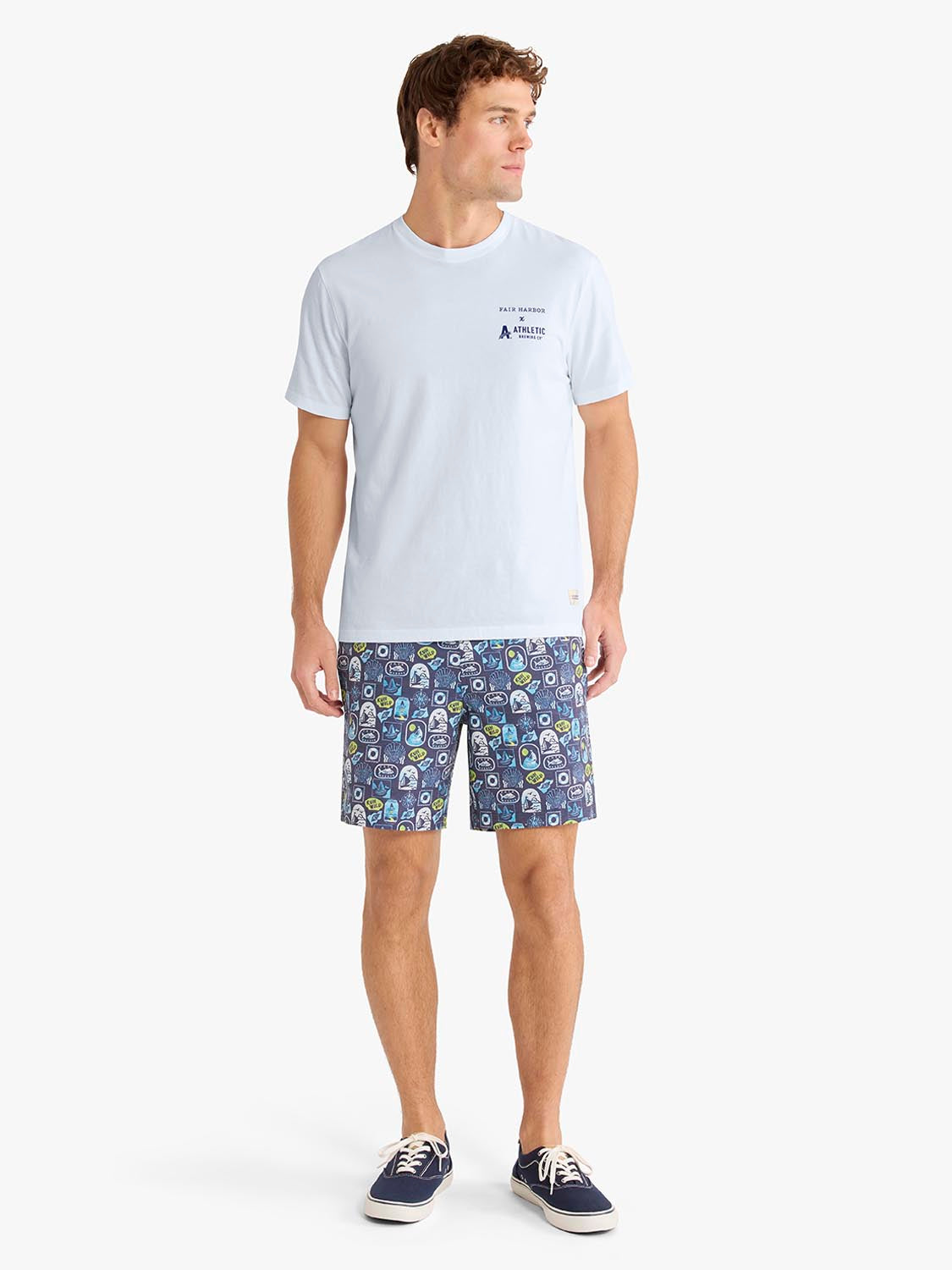 Man wearing light blue graphic tee with small chest logo and patterned navy shorts.