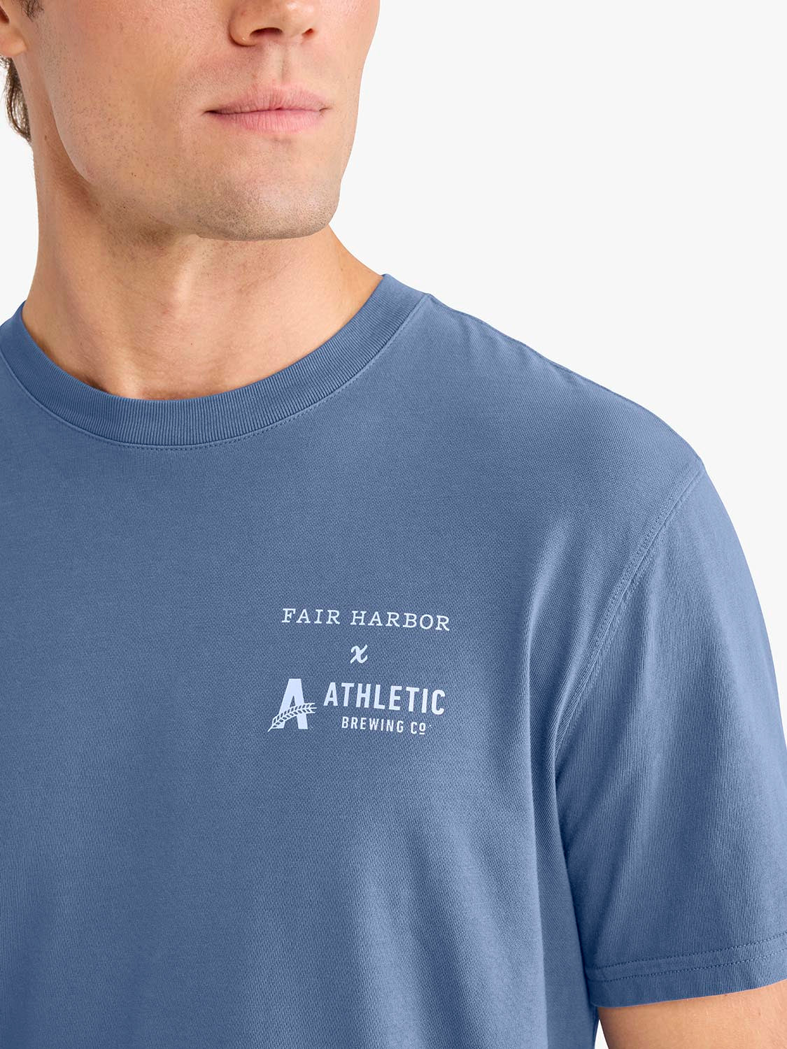 Man wearing a blue crew neck t-shirt with Fair Harbor and Athletic Brewing Co. text printed on chest.