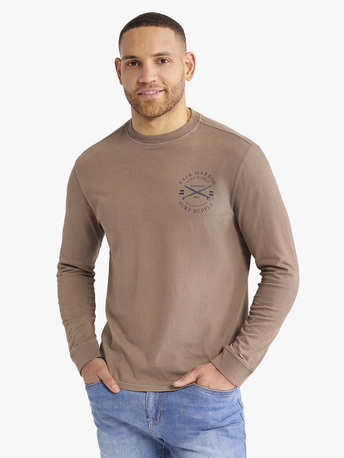 Man wearing a taupe long-sleeve graphic tee with an archival crest design on the chest.