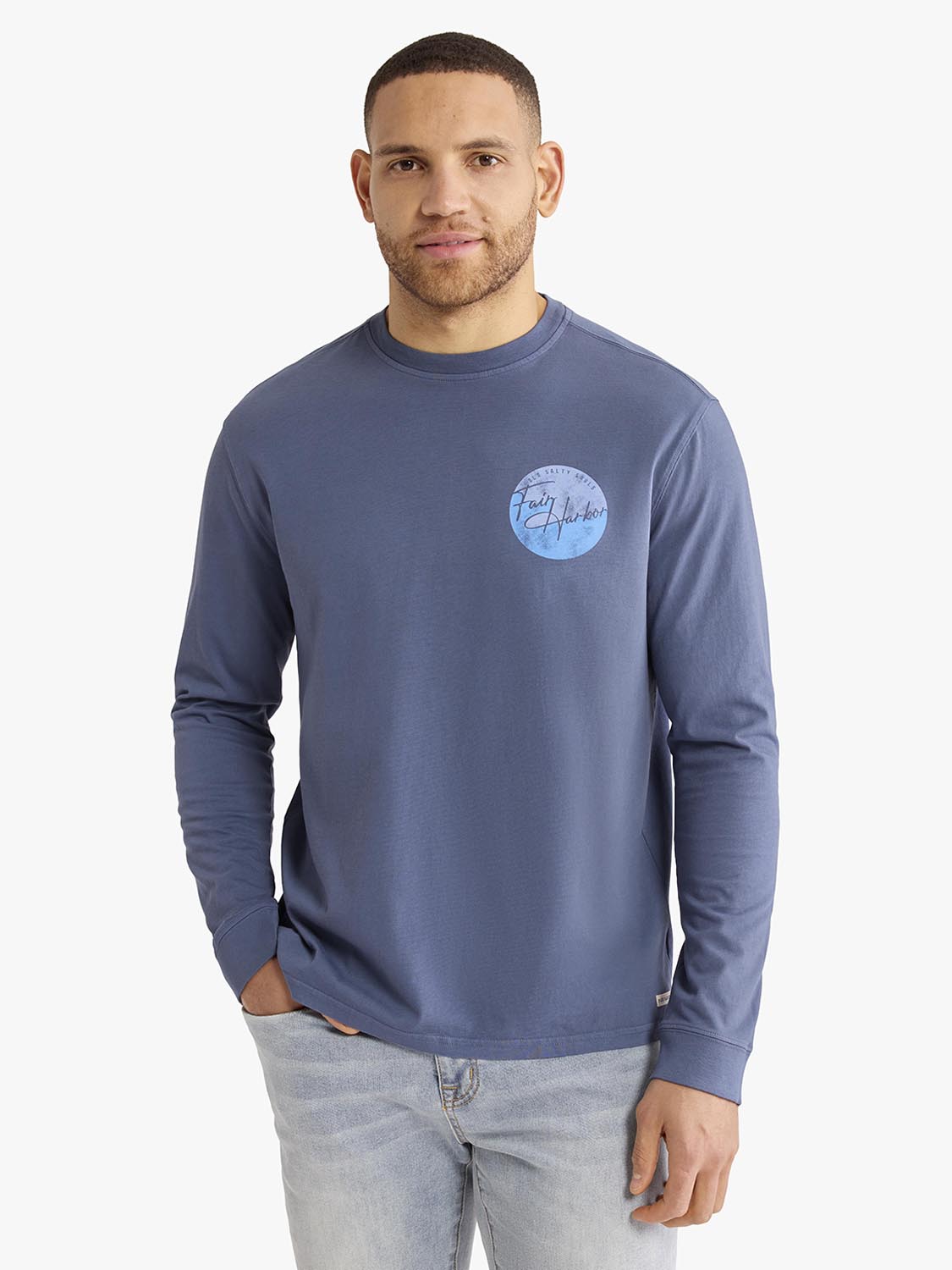 Man wearing a slate blue long sleeve graphic tee with a circular logo on the chest.