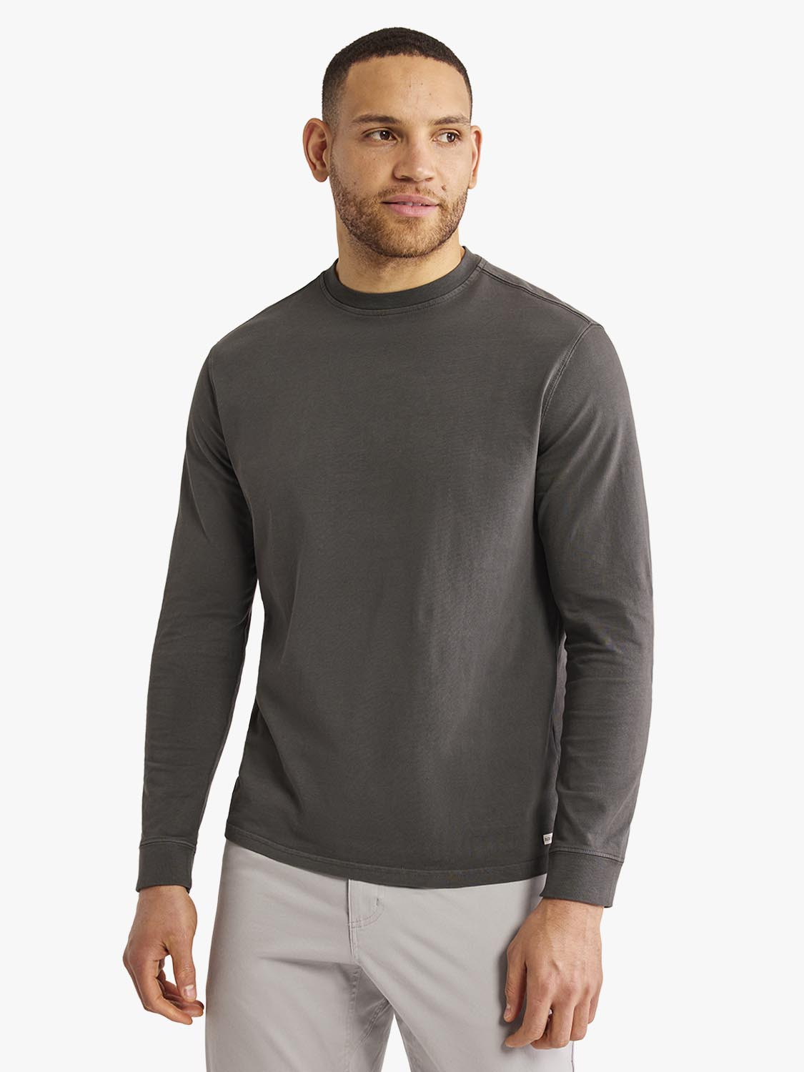 Man wearing a charcoal gray long sleeve crew neck tee with light gray pants.